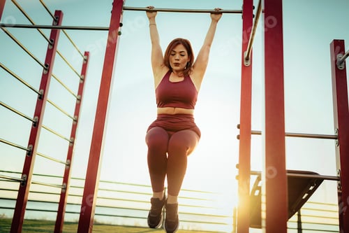 Preview: Strong woman doing pull-ups on horizontal bar showing effort and power