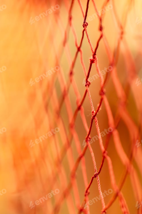 Preview: Closeup of a wired fence illuminated by an orange, hazy light