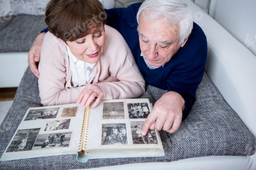 Preview: Senior couple lying on couch, looking at photo album