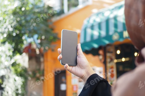 Preview: Woman holding smartphone in vibrant urban setting during daytime