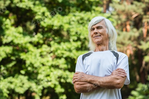 Preview: happy senior man in sportswear standing with crossed arms in green park