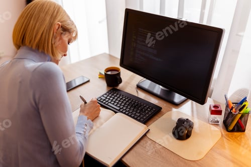 Preview: Woman writing notes while taking online programming course
