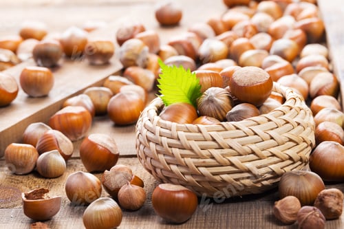 Preview: Hazelnuts arranged in a basket on a wooden table surrounded by scattered nuts