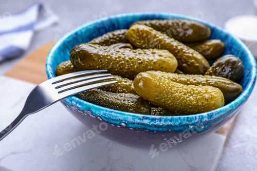 Preview: Fork with bowl of pickled cucumbers on light table, closeup