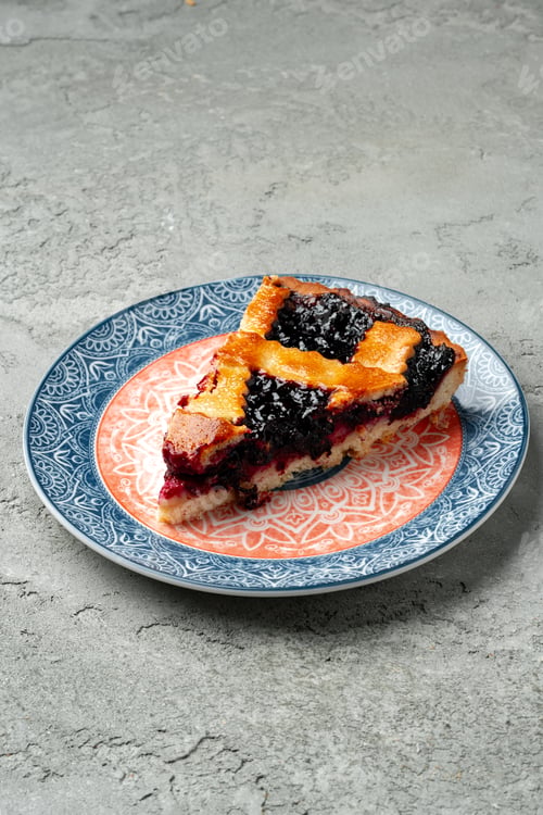 Preview: Slice of berry pie on a plate with decorative design placed on gray surface