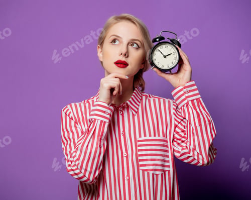 Preview: Beautiful woman in red striped shirt with alarm clock on purple background