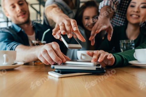 Preview: Young friends taking back their smartphones lying in pile on table in cafe
