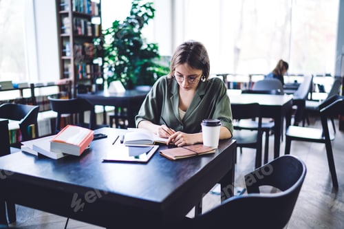 Preview: Diligent student in glasses writing in notepad