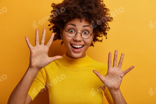 Preview: Horizontal shot of pleasant looking happy woman raises palms towards camera, has pleased cheerful ex