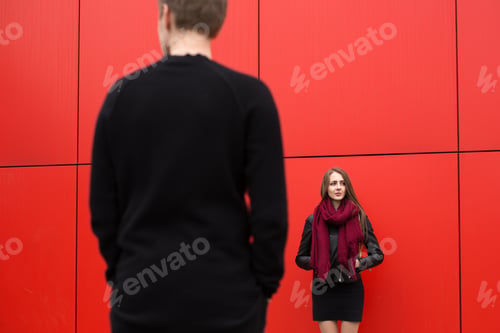 Preview: Young man and woman in passion, emotion, on the street with a backdrop of the red wall.