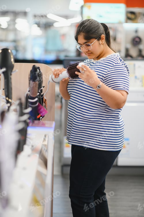 Preview: Beautiful indian woman in the store is testing a hairdryer