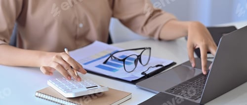 Preview: Cropped image of female accountant working with laptop computer and using calculator.