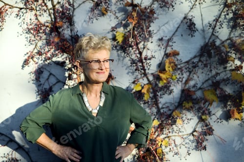 Preview: Senior woman standing outdoors against wall in town.