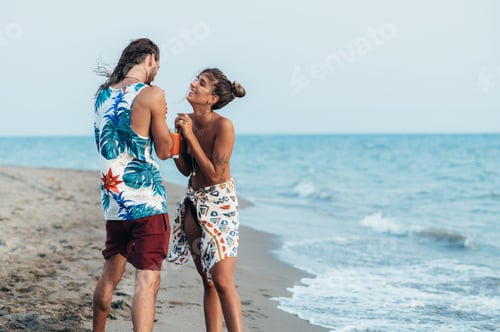 Preview: Attractive young couple with alcohol cocktails walking on the beach