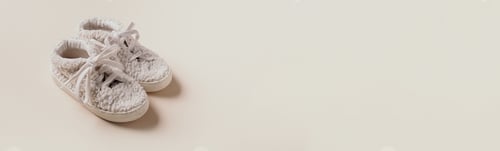 Preview: Gender neutral baby teddy shoes and accessories over beige background. Top view, copy space