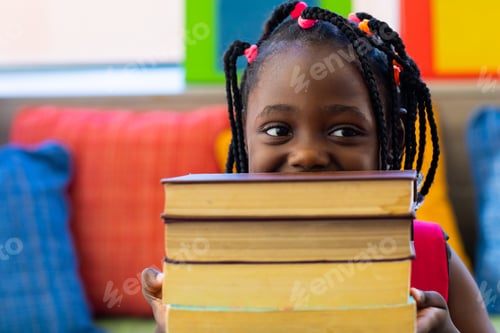 Preview: Happy african american schoolgirl holding books in colourful room at elementary school
