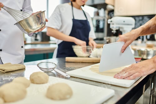 Preview: cropped view of female chef cutting dough next to young colleague and chief cook, confectionery