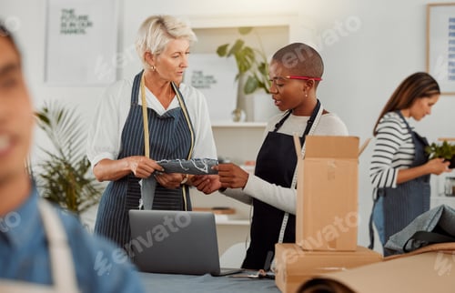 Preview: Two clothing designers using a laptop while working with material in a meeting at work. Young femal