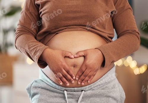 Preview: Heart hands on belly, pregnant mother and closeup of happy black woman alone in Africa living room.