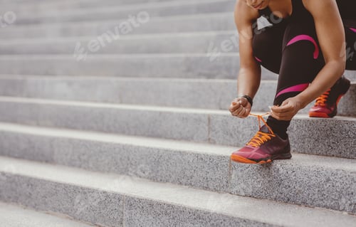 Preview: Urban activity. African american woman in sportswear tying laces on sneakers for workout
