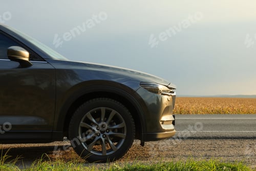 Preview: Black modern car parked on roadside at sunset, closeup. Space for text