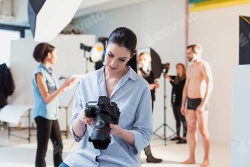 Preview: Young female photographer reviewing shoot on digital SLR in photography studio