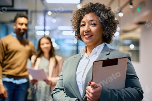 Preview: Smiling real estate agent in the office with her clients in the background.