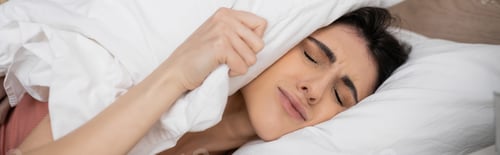 Preview: Displeased woman putting pillow on head on bed in morning, banner