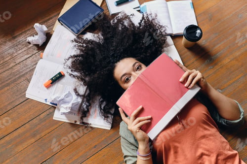 Preview: Student girl with dark curly hair lying on floor with textbooks around dreamily looking in camera