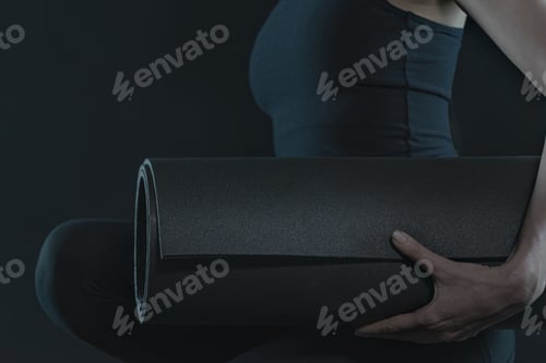 Preview: Young woman with yoga mat practicing yoga on dark black background. close up