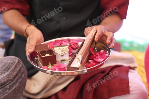Preview: Closeup of a person holding golden jewelry gifts with rose petals during an Indian wedding