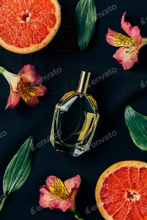 Preview: top view of bottle of perfume surrounded with alstroemeria flowers and grapefruit slices on black
