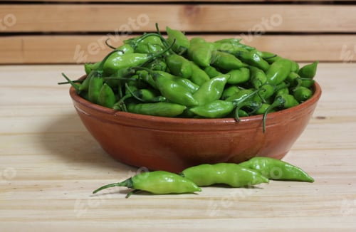 Preview: Bowl of fresh green aji limo chili peppers on a wooden table.