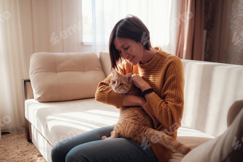 Preview: Young woman resting with pet in sofa at home.