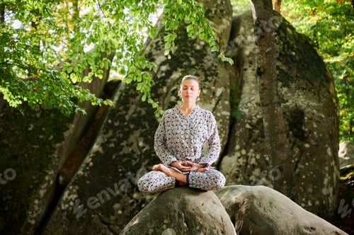 Preview: Woman practicing yoga outdoors in forest. Barefoot female on yoga mat surrounded by trees and rocks