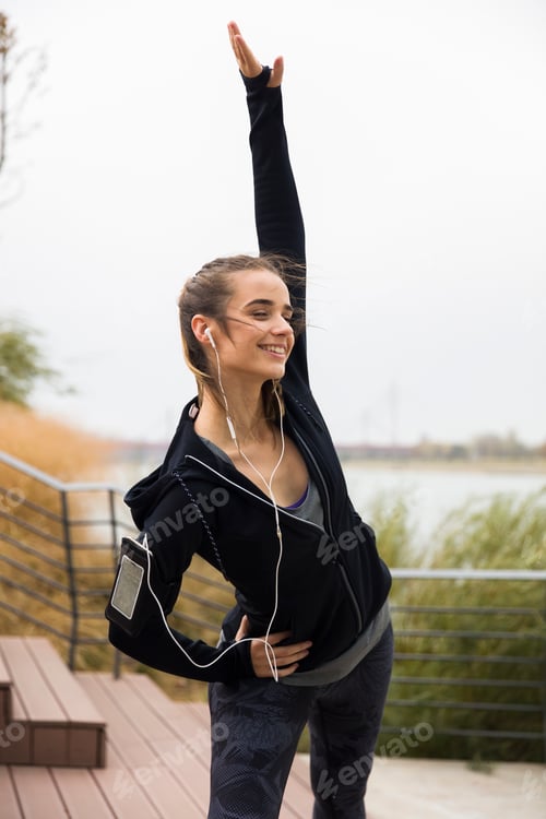 Preview: Female athlete stretching her arms while listening to music outdoors