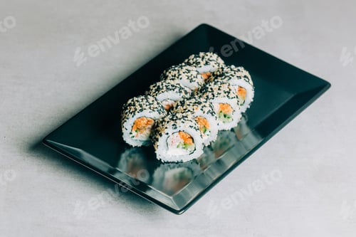 Preview: sushi rolls in sesame with salmon on black plate on gray background