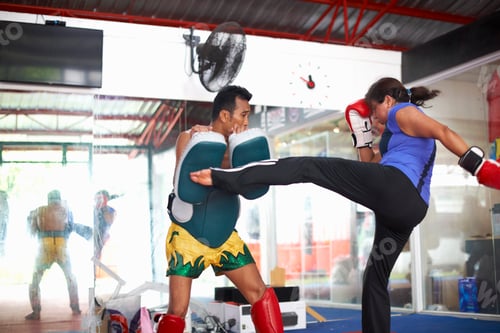 Preview: Mature woman practicing kickboxing with male trainer in gym