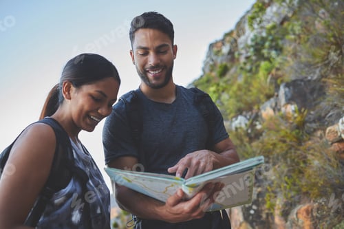 Preview: Shot of a young couple using a guide book to complete a hike in a mountain range