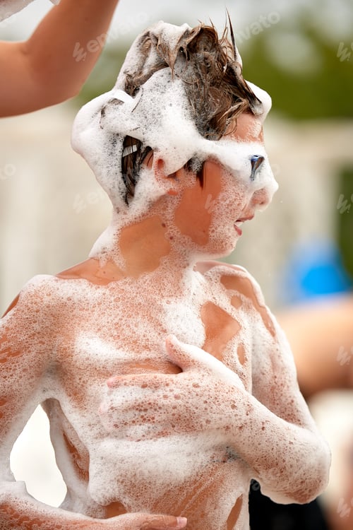 Preview: Happy little boy with goggles and foam on his head having fun in a water park, in wet swimwear at a