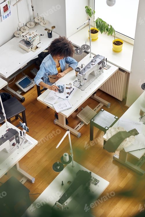 Preview: African-American woman designer looks at drawing by sewing machine shooting video in studio