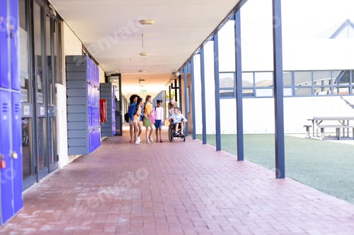 Preview: Diverse group of school children walking in school corridor talking, one in wheelchair, copy space