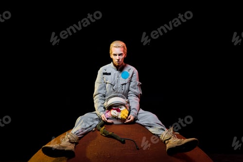 Preview: attractive female astronaut in spacesuit with flowers in helmet sitting on planet