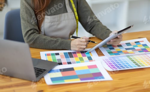 Preview: Fashion designer in design studio working with laptop and fabric color samples on desk.