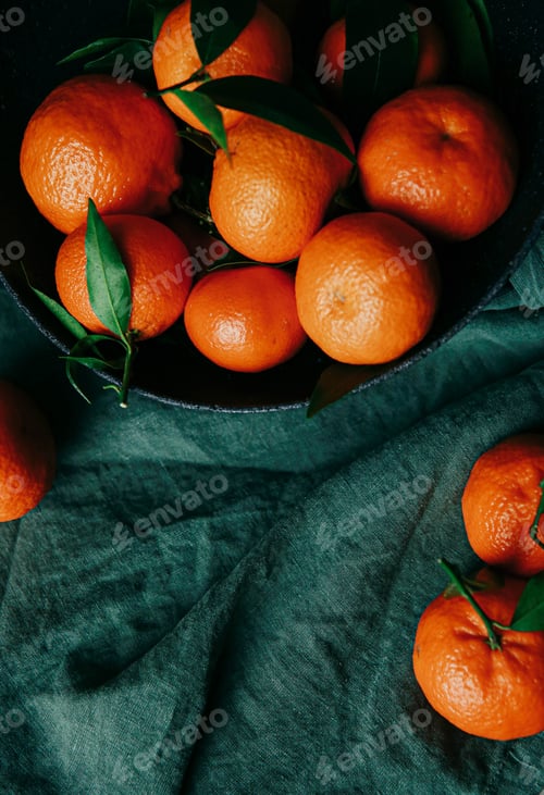 Preview: delicious tangerines with a bowl of black stone on a textured green fabric