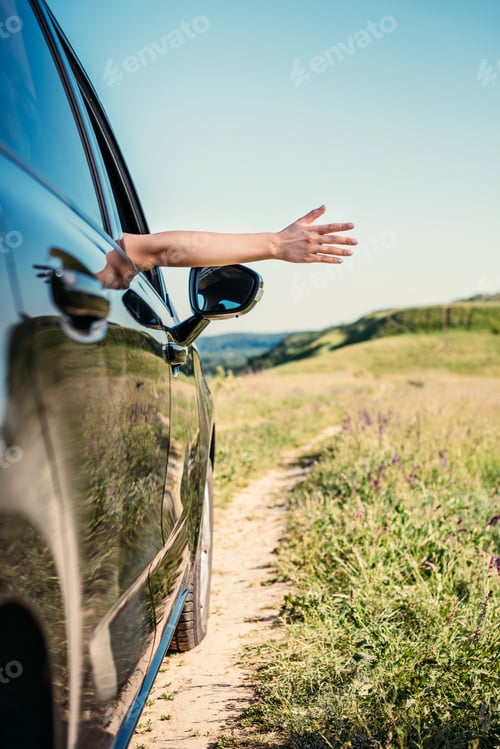 Preview: cropped shot of woman leaning out hand from car window in rural field