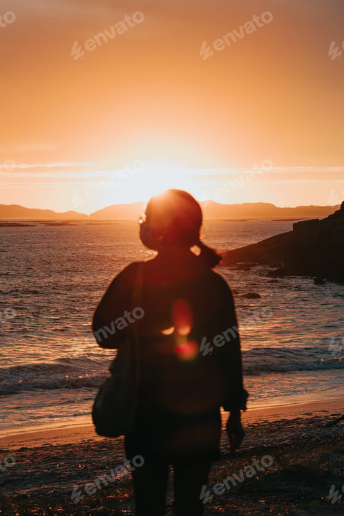 Preview: A traveler in front of a colorful sunset in the beach wearing a face mask, wellness concept