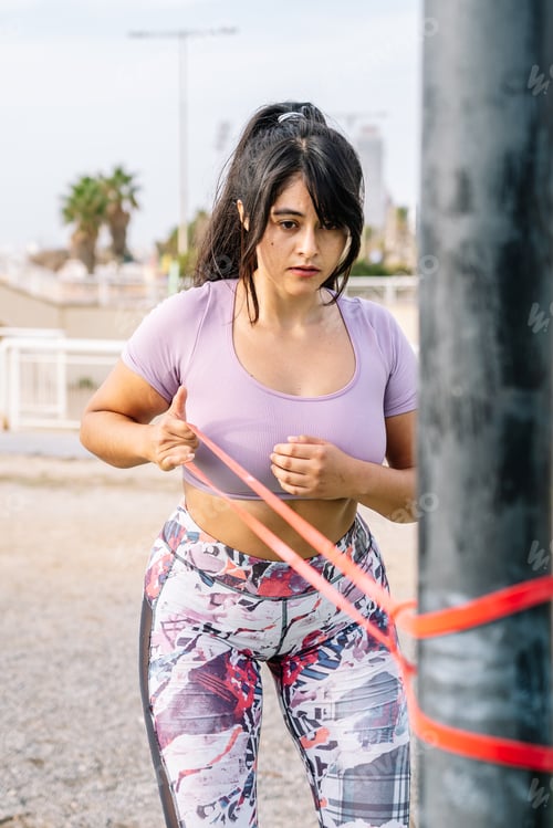 Preview: Fit young female athlete exercising with resistance band on beach