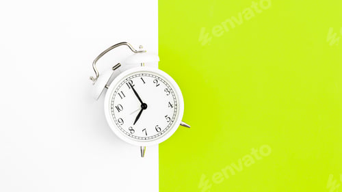 Preview: White alarm clock on a white and green background, flat lay.