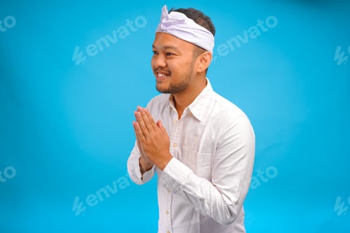 Preview: Handsome young Balinese man wearing Indonesian traditional udeng doing greeting or welcome gesture.